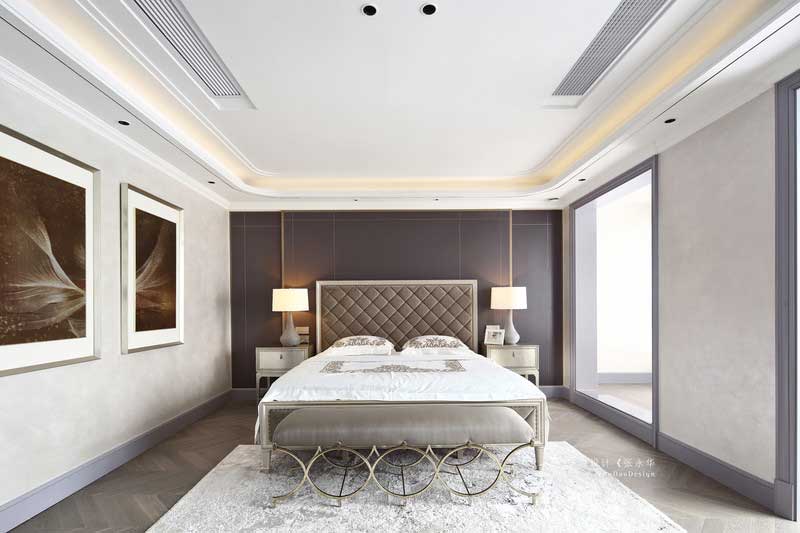 三樓是整個主臥空間，擁有內(nèi)門廳、主臥室、衣帽間、衛(wèi)生間等。主臥背景選用深灰色的硬包裝飾，加上金屬線條的點綴，讓整個背景不顯呆板。主臥陽臺同樣打通與臥室形成一體，局部空間做了地臺，讓整個空間既寬敞又有層次。